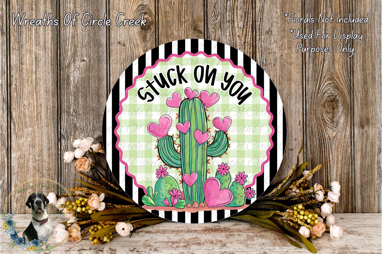 a decorative sign with a cactus and hearts, surrounded by flowers and placed on a wooden surface.