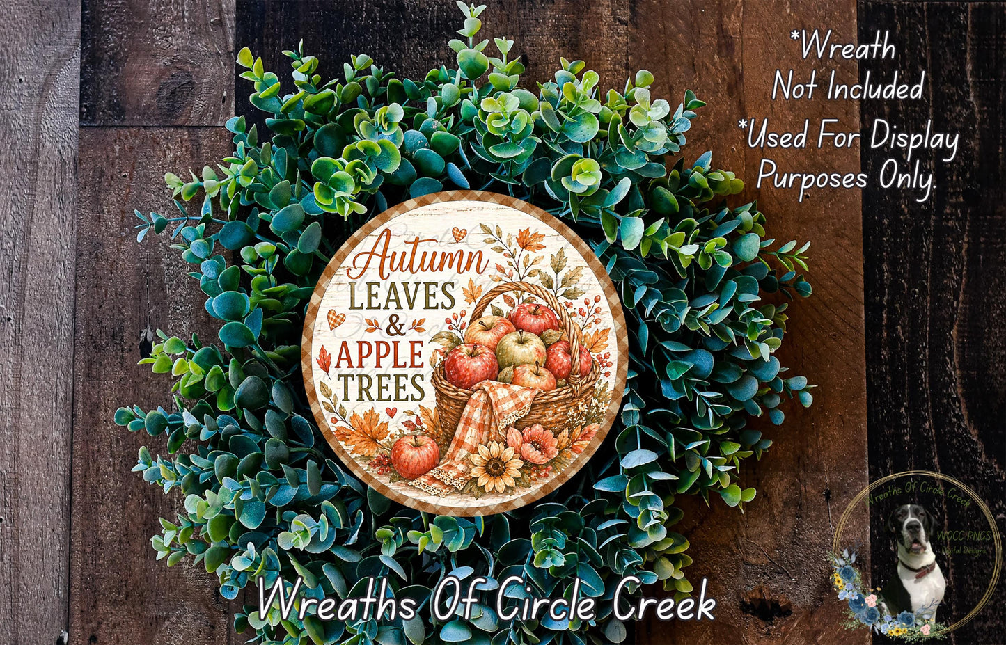 a wreath made of various autumn leaves and apples, with a sign that reads "Autumn Leaves & Apple Trees" in the center. The wreath is displayed on a wooden surface, and there is a small dog in the bottom right corner of the image.