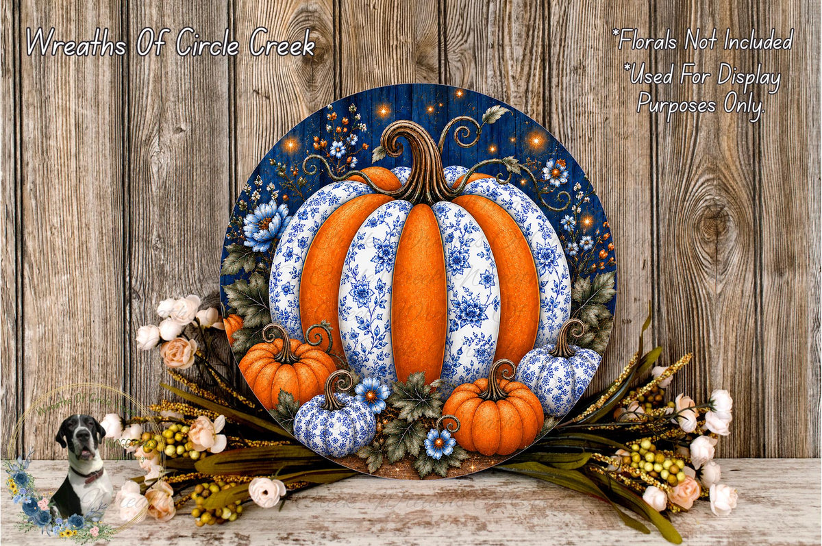 A decorative wreath featuring a large orange pumpkin surrounded by smaller pumpkins, flowers, and leaves, set against a wooden background.