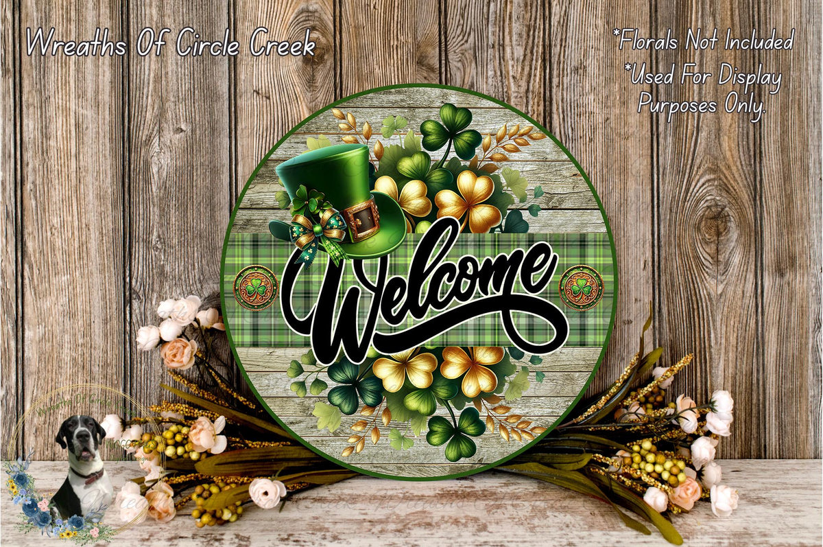 a circular sign with a welcoming message, surrounded by a variety of flowers and greenery. The sign has a green hat and a green plaid pattern, and the word "Welcome" is prominently displayed in the center.