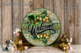 a circular sign with a welcoming message, surrounded by a variety of flowers and greenery. The sign has a green hat and a green plaid pattern, and the word "Welcome" is prominently displayed in the center.