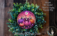 A Halloween-themed wreath made of green foliage and colorful pumpkins, with a spider web and a full moon in the background.