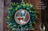 A wreath made of green foliage and a red bow, featuring a deer in a snowy forest scene.