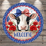 A cow wearing a patriotic bow tie is surrounded by red roses and American flags, with the word "Welcome" written below.