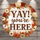 A circular sign with the text "YAY! you're here" surrounded by a wreath of autumn flowers and leaves.