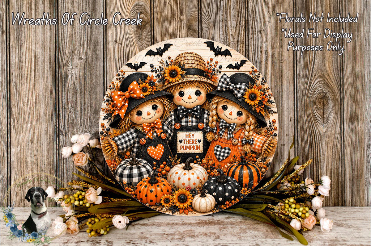 A decorative wreath featuring three scarecrow dolls, pumpkins, and flowers, with the text "Hey there Pumpkin" displayed on the wreath.