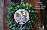 a wreath made of green plants and a pink wagon with a cartoon rabbit and carrots on the back. The wreath is displayed on a wooden surface, and there is a text overlay that reads "Wreath Not Included * Used For Display Purposes Only".