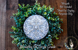A wreath made of green leaves and a silver snowflake ornament, placed on a wooden surface.