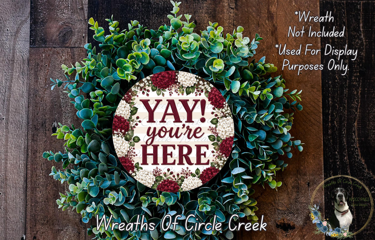 a wreath made of various green and red foliage, with a large circular sign in the center that says "YAY! you're here".