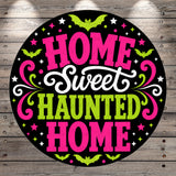 a circular graphic with the text "HOME Sweet Haunted Home" in a stylized font, surrounded by decorative elements such as bats, stars, and swirls in pink, green, and white colors.