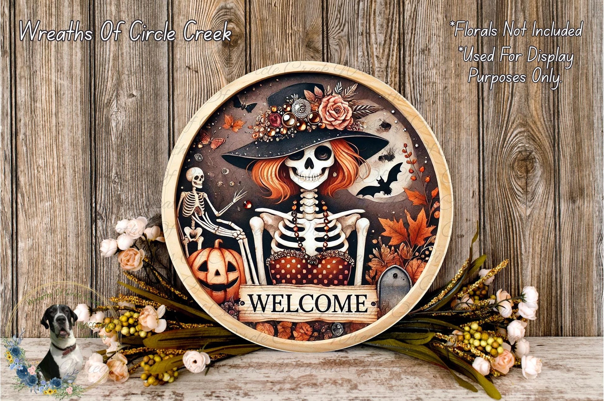 a decorative wreath with a skeleton wearing a hat and holding a pumpkin, surrounded by flowers and leaves. The wreath has the word "WELCOME" written on it.