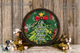 A circular wooden sign with a Christmas tree design, surrounded by flowers and placed on a wooden surface.