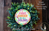 a wreath made of green leaves and a colorful sign that reads "Fight Cancer in all Colors". The wreath is displayed on a wooden surface, and there is a small dog in the bottom right corner of the image.