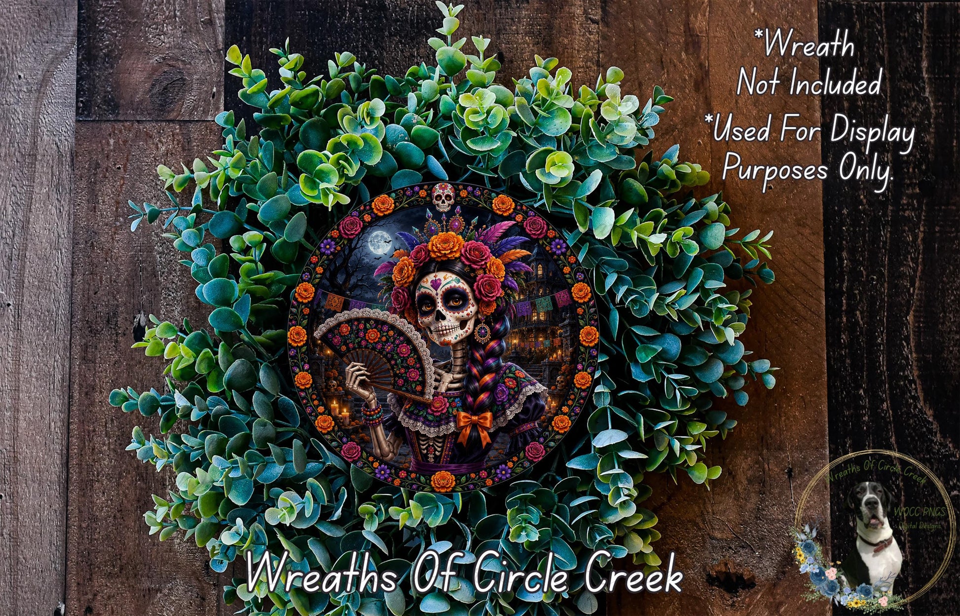 A wreath featuring a colorful design of a skeleton wearing a headdress, surrounded by green foliage and flowers. The wreath is displayed on a wooden surface.