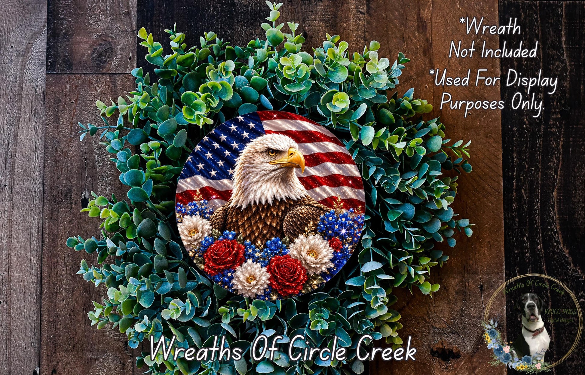 a wreath with an American flag design, surrounded by greenery and flowers. The wreath is displayed on a wooden surface, and there is a small dog in the bottom right corner of the image.