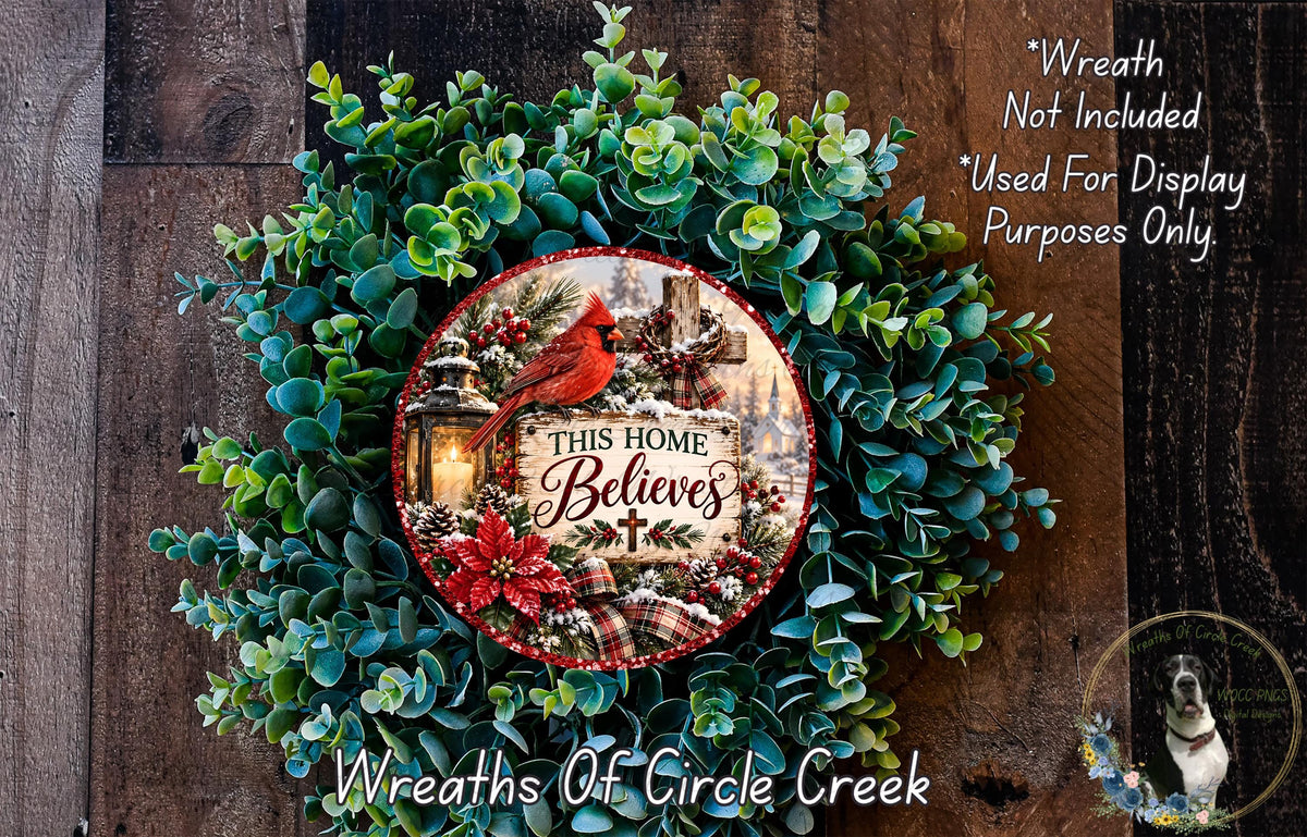 a wreath made of green leaves and a red cardinal bird, with a sign that reads "This Home Believes" in the center. The wreath is displayed on a wooden surface, and there is a small dog in the bottom right corner.