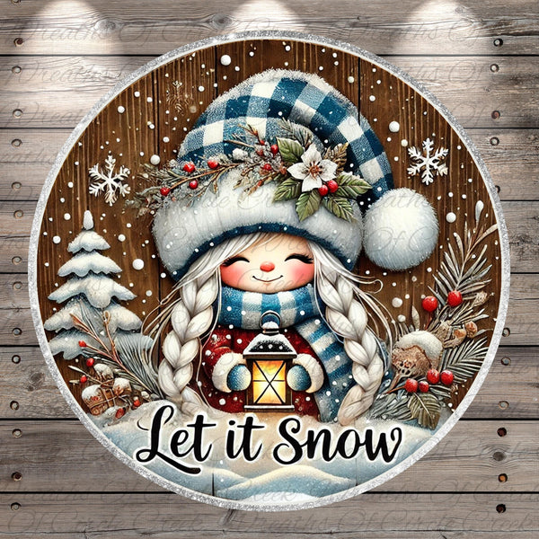 A round, wooden sign with a smiling girl wearing a blue and white hat and holding a lantern, surrounded by snowflakes, pine trees, and berries. The sign has the text "Let it Snow" written on it.