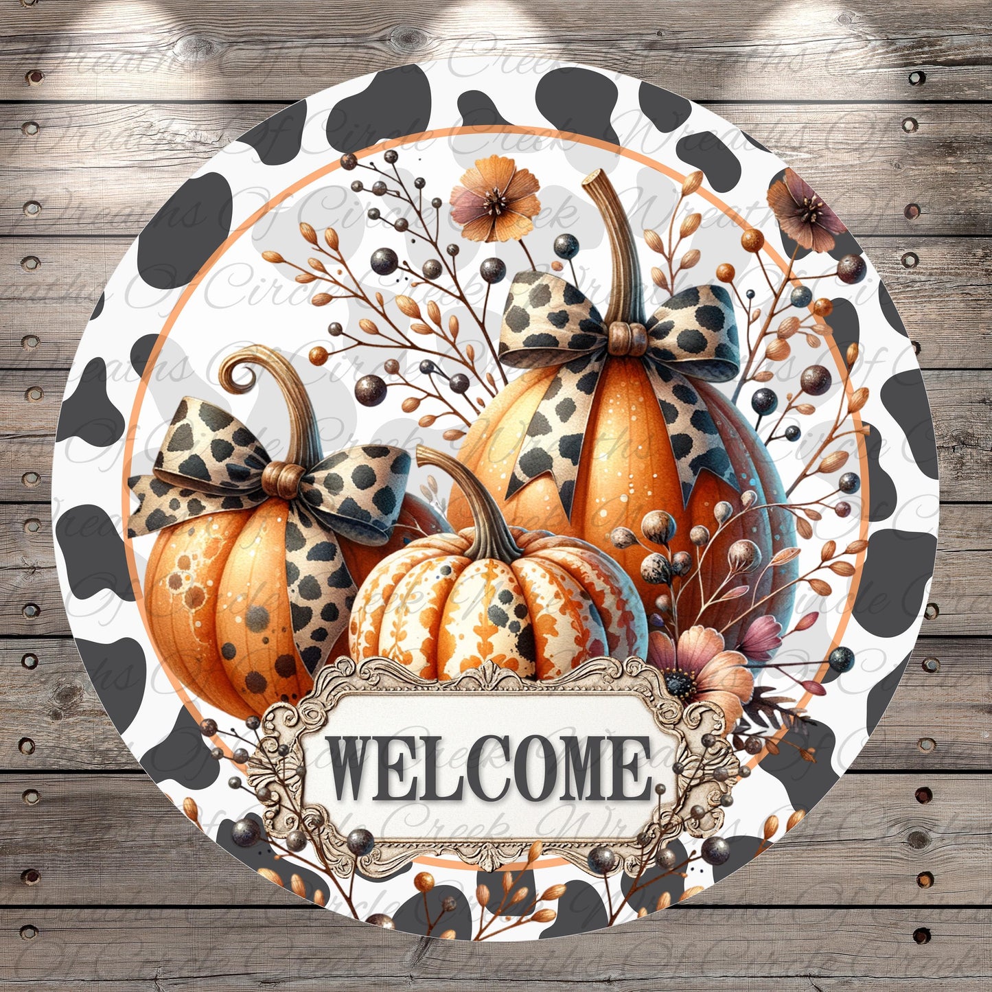 A circular welcome sign featuring three decorative pumpkins with bows, surrounded by fall foliage and flowers. The sign has a black and white spotted pattern and the word "WELCOME" is displayed in the center.