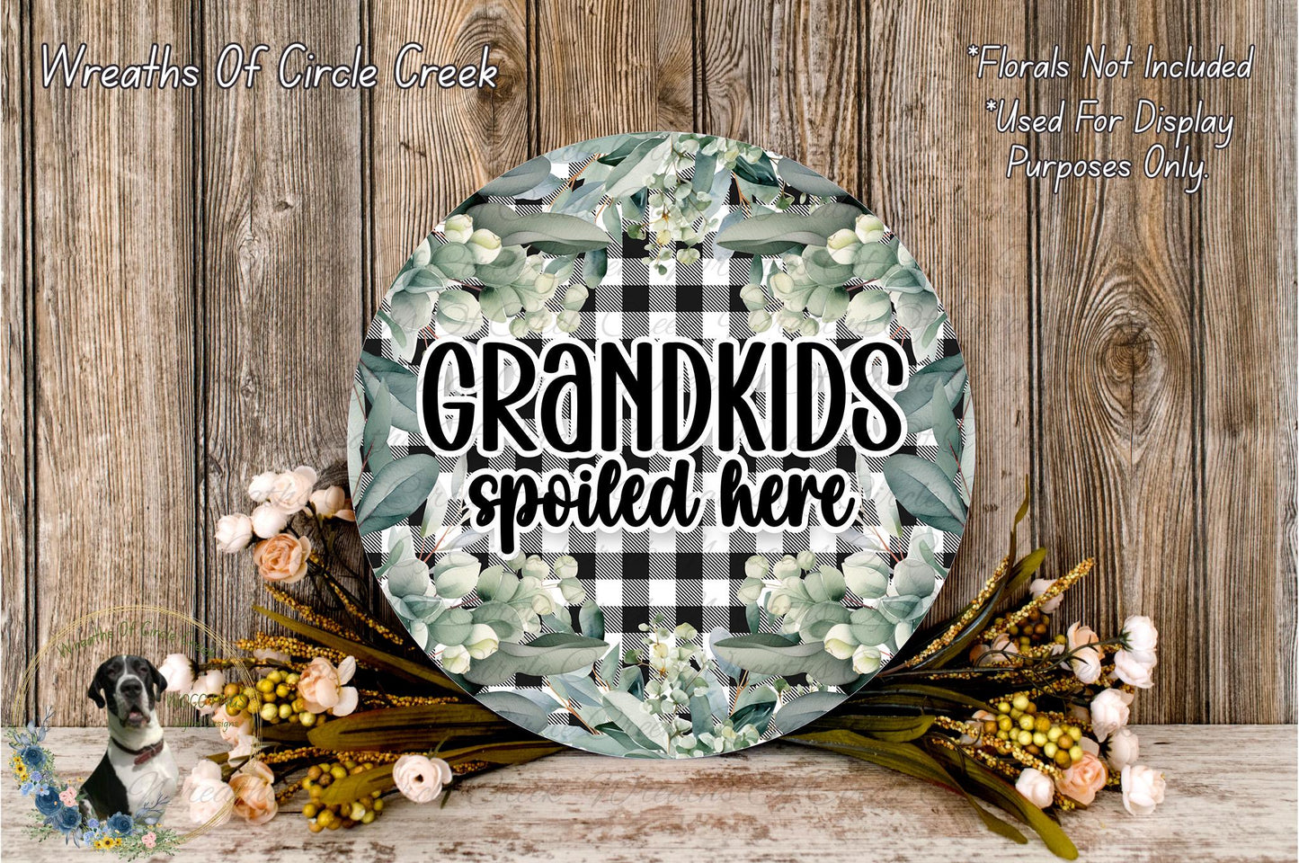 a round sign with the text "GRANDKIDS spoiled here" surrounded by a floral arrangement and some flowers.
