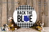 a round sign with the text "BACK THE BLUE" displayed prominently in the center. The sign is surrounded by a wreath of flowers and a wooden background.