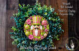 A wreath made of green and pink flowers, with a nutcracker figure in the center, is displayed on a wooden surface.
