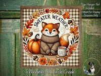 The image is a decorative wreath featuring a fox wearing a sweater and surrounded by autumn elements such as pumpkins, leaves, and flowers. The fox is sitting on a shelf with a cup of coffee and a book.