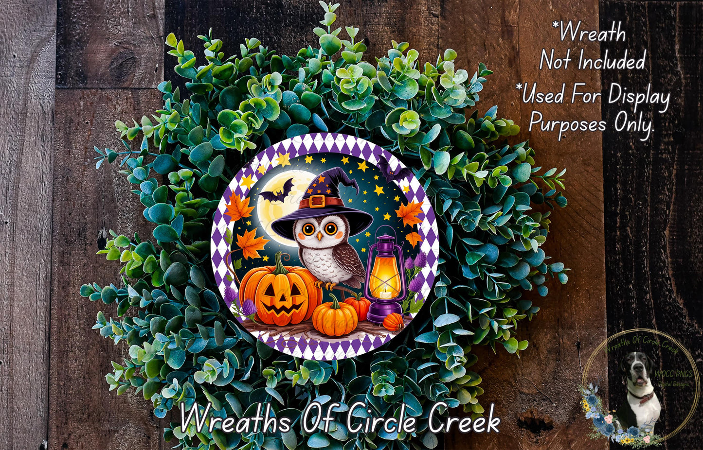 A Halloween-themed wreath made of green foliage, featuring an owl, jack-o-lanterns, and a lantern, with a wooden background.