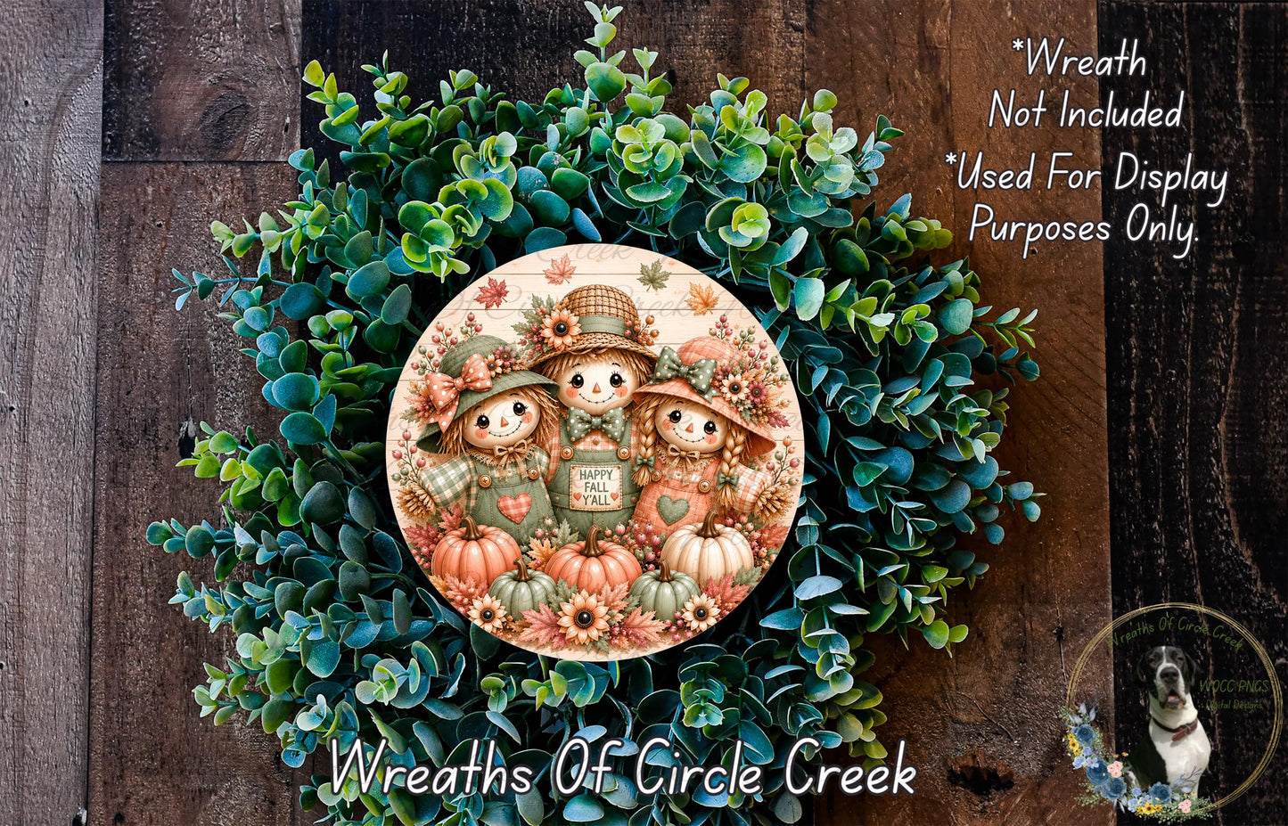 a wreath with a central design of three scarecrow characters surrounded by autumn foliage and pumpkins. The wreath is displayed on a wooden surface, and there is a small dog visible in the bottom right corner of the image.
