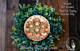 a wreath with a central design of three scarecrow characters surrounded by autumn foliage and pumpkins. The wreath is displayed on a wooden surface, and there is a small dog visible in the bottom right corner of the image.
