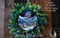 A wreath made of green leaves and a circular design featuring a winter village scene, with a blue sky and stars above.
