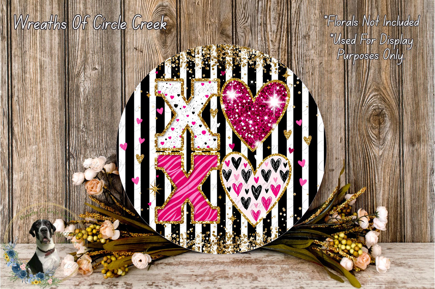 a decorative round sign with a black and white striped background, adorned with pink and white hearts and glitter accents. The sign is surrounded by a floral arrangement of flowers, creating a visually appealing and festive display.