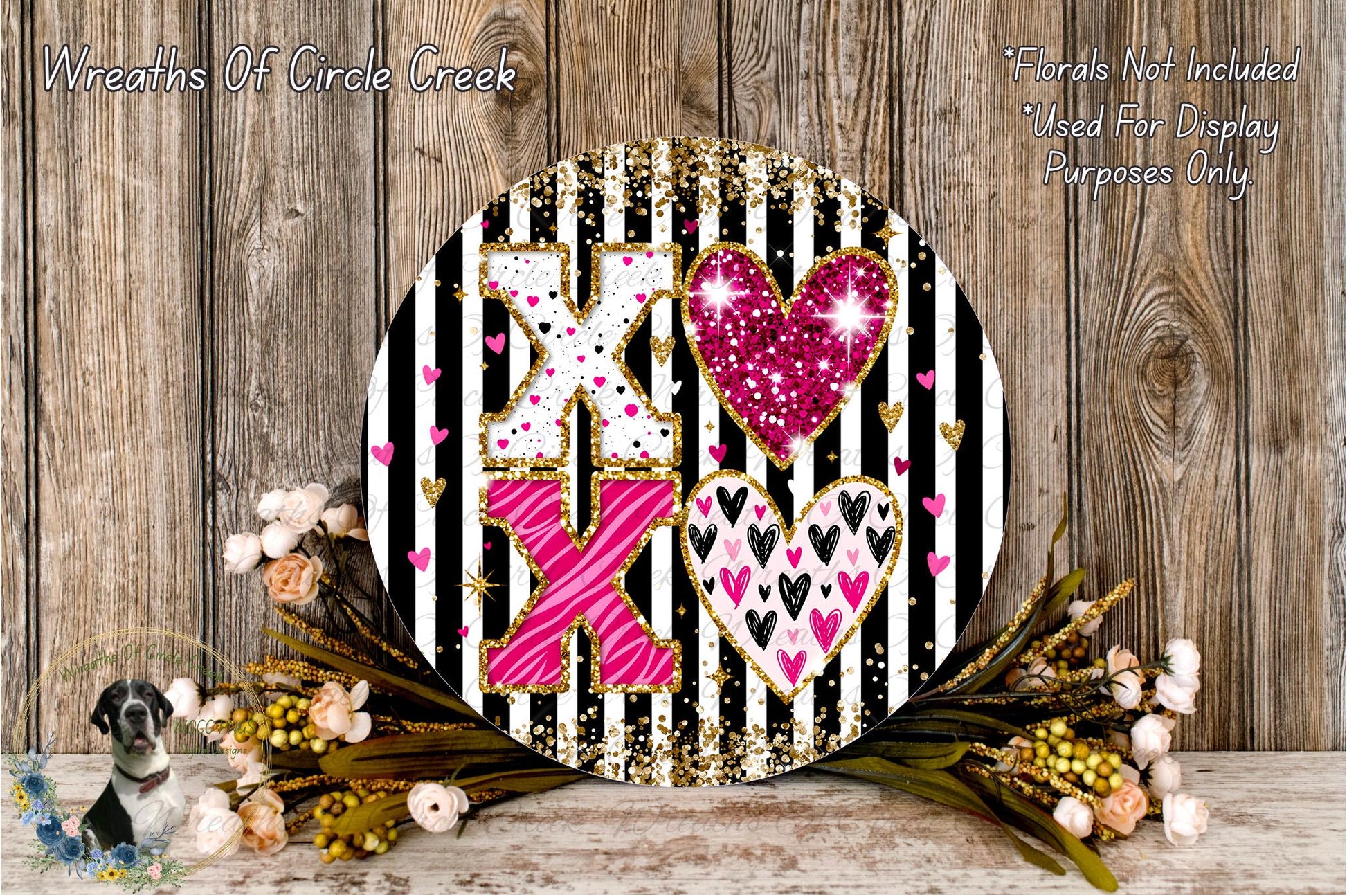 a decorative round sign with a black and white striped background, adorned with pink and white hearts and glitter accents. The sign is surrounded by a floral arrangement of flowers, creating a visually appealing and festive display.