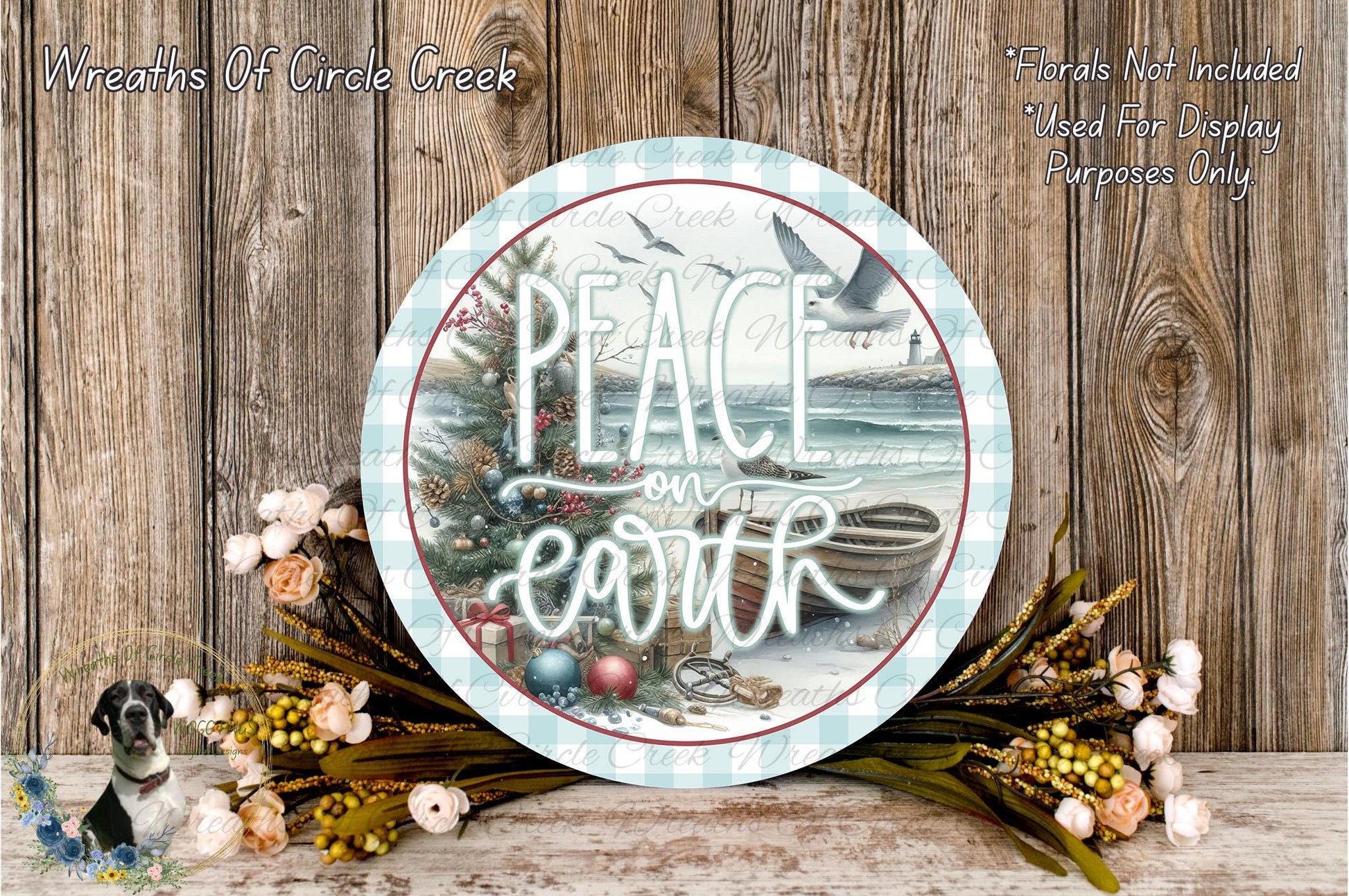 a circular sign with the text "Peace on earth" written on it, surrounded by a wreath of flowers and a small boat. The sign is placed on a wooden surface, and there are additional floral arrangements in the background.