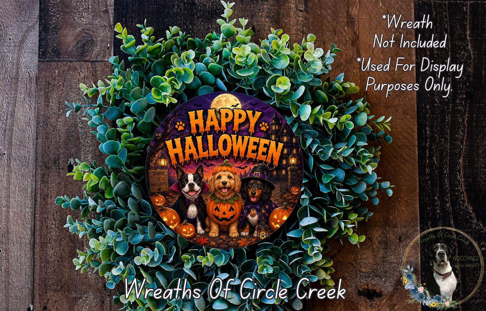 A Halloween wreath made of green leaves and featuring a dog, cat, and pumpkin. The wreath has the text "Happy Halloween" and is displayed on a wooden background.