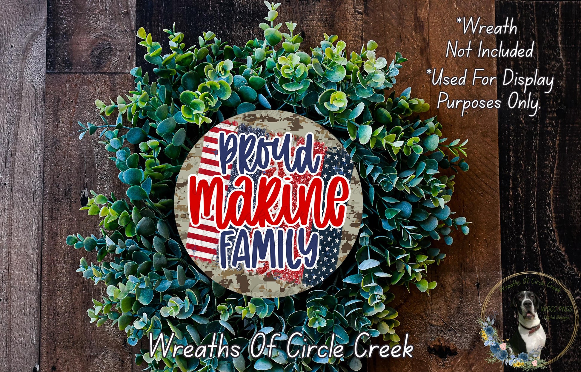 a wreath made of green leaves and a circular sign with the text "Proud Marine Family" in red and blue colors. The wreath is displayed on a wooden surface, and there is a small dog in the bottom right corner of the image.