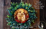 A wreath with a circular design featuring a depiction of the Virgin Mary, baby Jesus, and the Holy Family, surrounded by greenery and red roses.