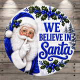 Santa Claus with his hand over his mouth, surrounded by holly leaves, berries, and the text "We believe in Santa".