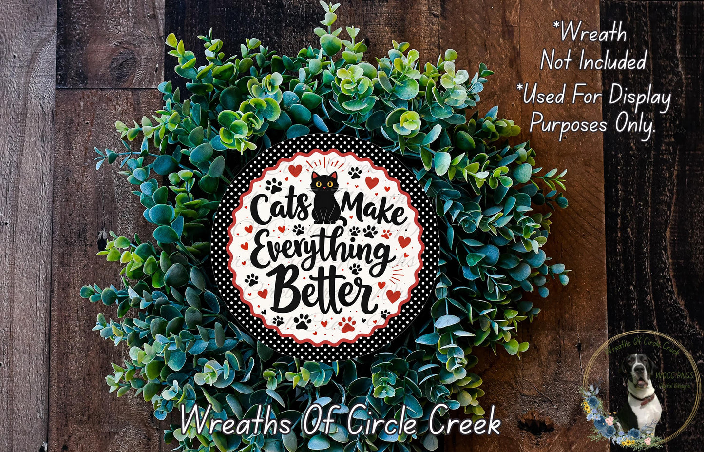 A wreath made of green leaves and a circular sign with the text "Cats Make Everything Better" is displayed on a wooden surface.