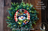 A wreath featuring a snowman with a red scarf and a bird perched on its head, surrounded by a lush green wreath.