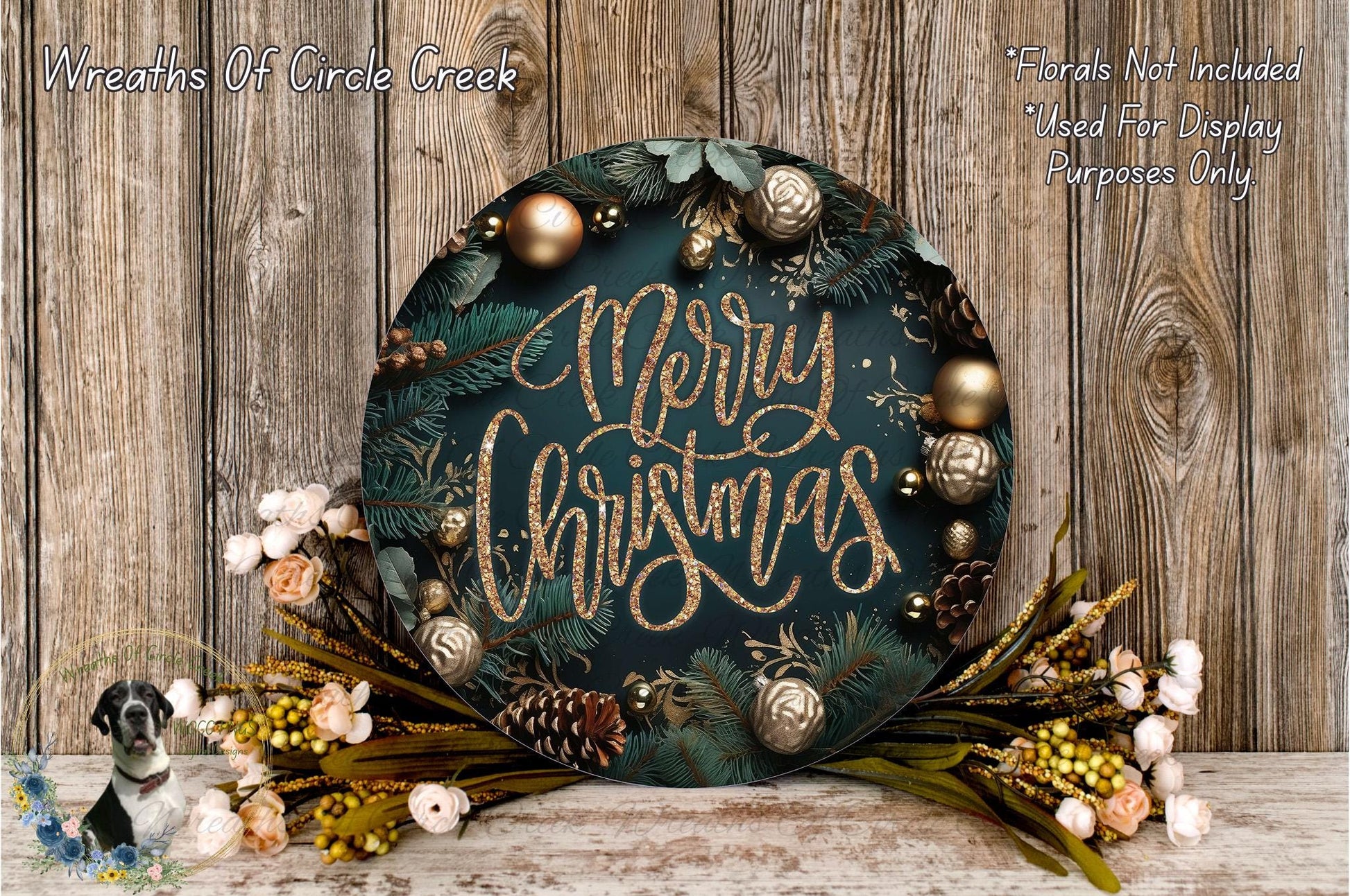 A festive Christmas wreath with the text "Merry Christmas" displayed on it, surrounded by various holiday decorations such as pine cones, pine branches, and ornaments. The wreath is placed on a wooden surface, and there are also some flowers and greenery surrounding it.