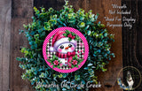 A wreath made of green foliage and a pink snowman with a red scarf and hat, placed on a wooden surface.