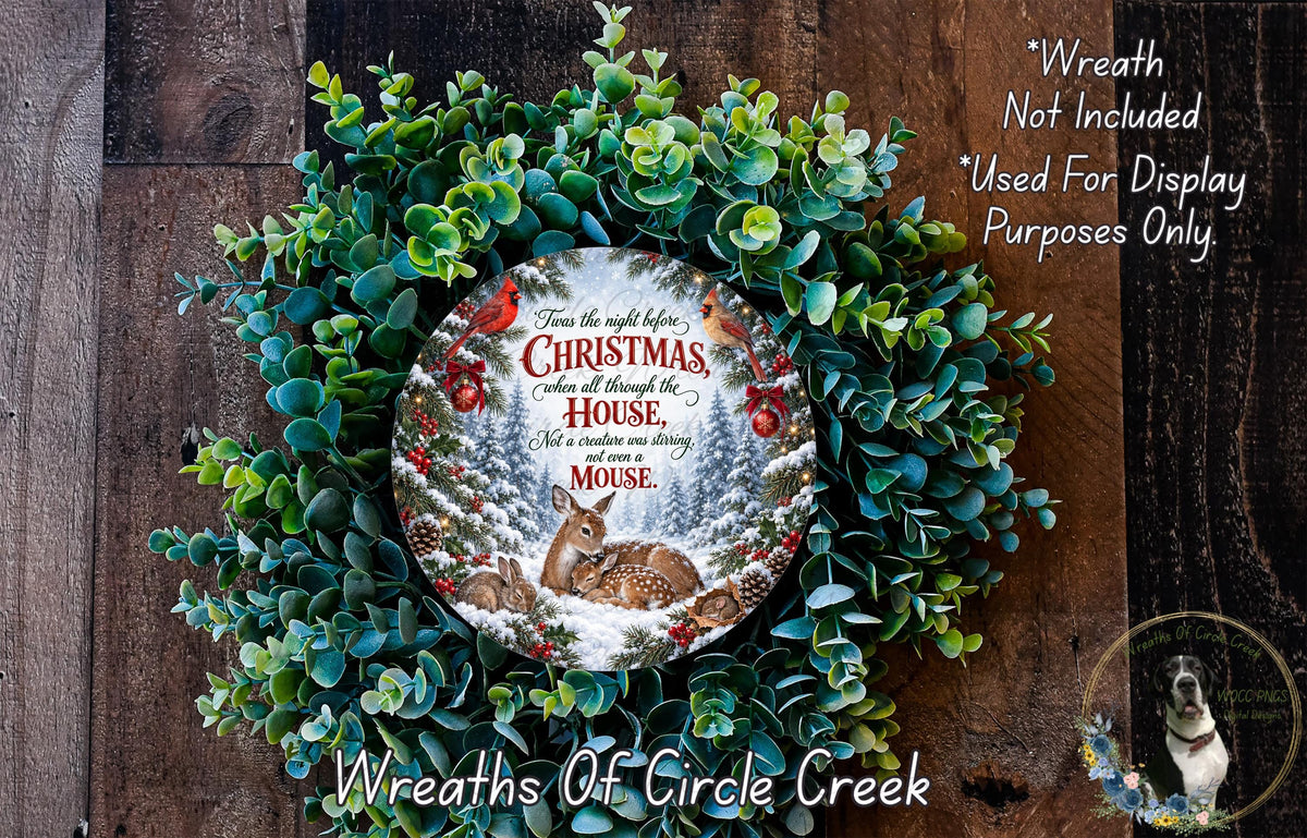 a Christmas wreath with a deer and pine tree design, surrounded by greenery. The wreath is displayed on a wooden surface, and there is a small dog in the bottom right corner.