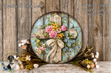 A round wooden cross adorned with a floral arrangement, including pink and yellow flowers, is displayed against a rustic wooden background.