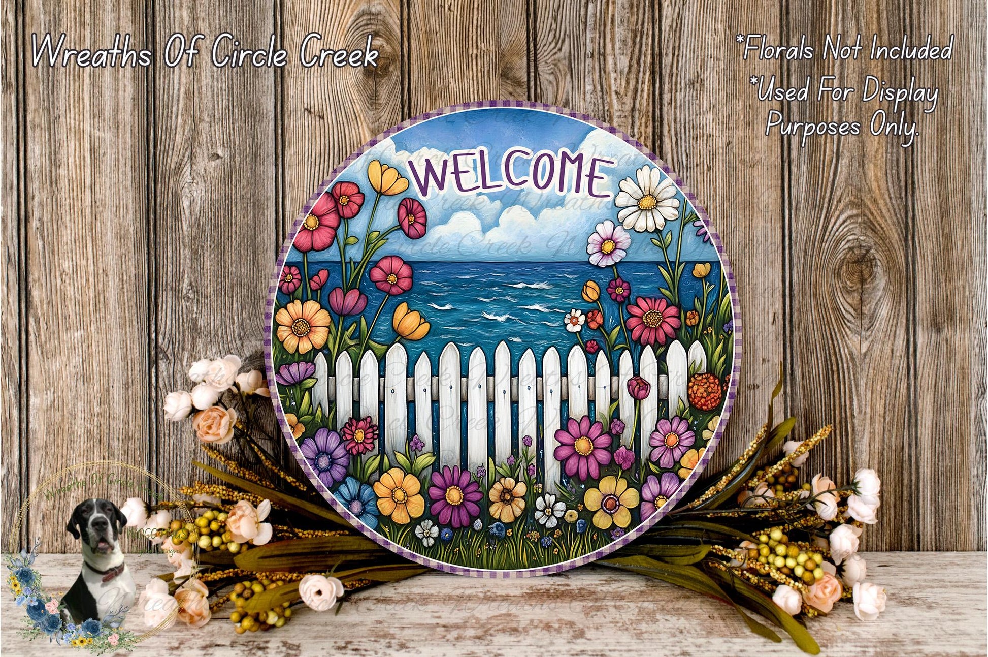 a round sign with a colorful floral design, surrounded by a wreath of flowers and a white picket fence. The sign displays the word "WELCOME" and is placed on a wooden surface.