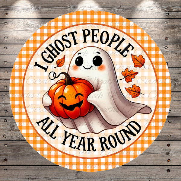 A round, orange and white sign with a cartoon ghost holding a pumpkin and the text "I ghost people all year round"