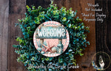 a wreath with a sign that says "Welcome" in the center, surrounded by various greenery and a starfish. The wreath is displayed on a wooden surface, and there is a small dog in the bottom right corner of the image.