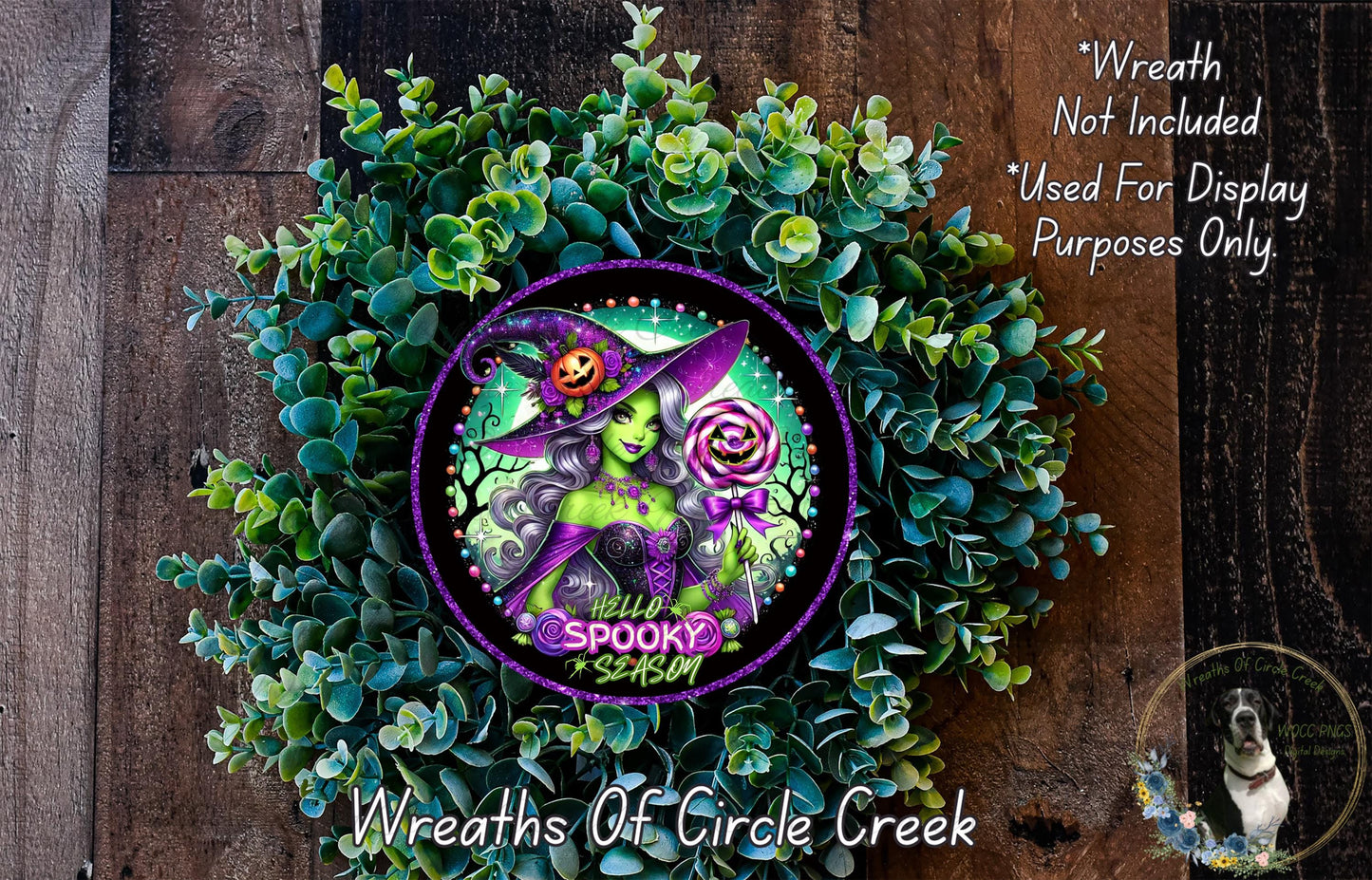 a wreath with a witch on it, surrounded by greenery. The wreath has a purple border and a purple and green design. The text above the wreath says "Wreath Not Included * Used For Display Purposes Only".