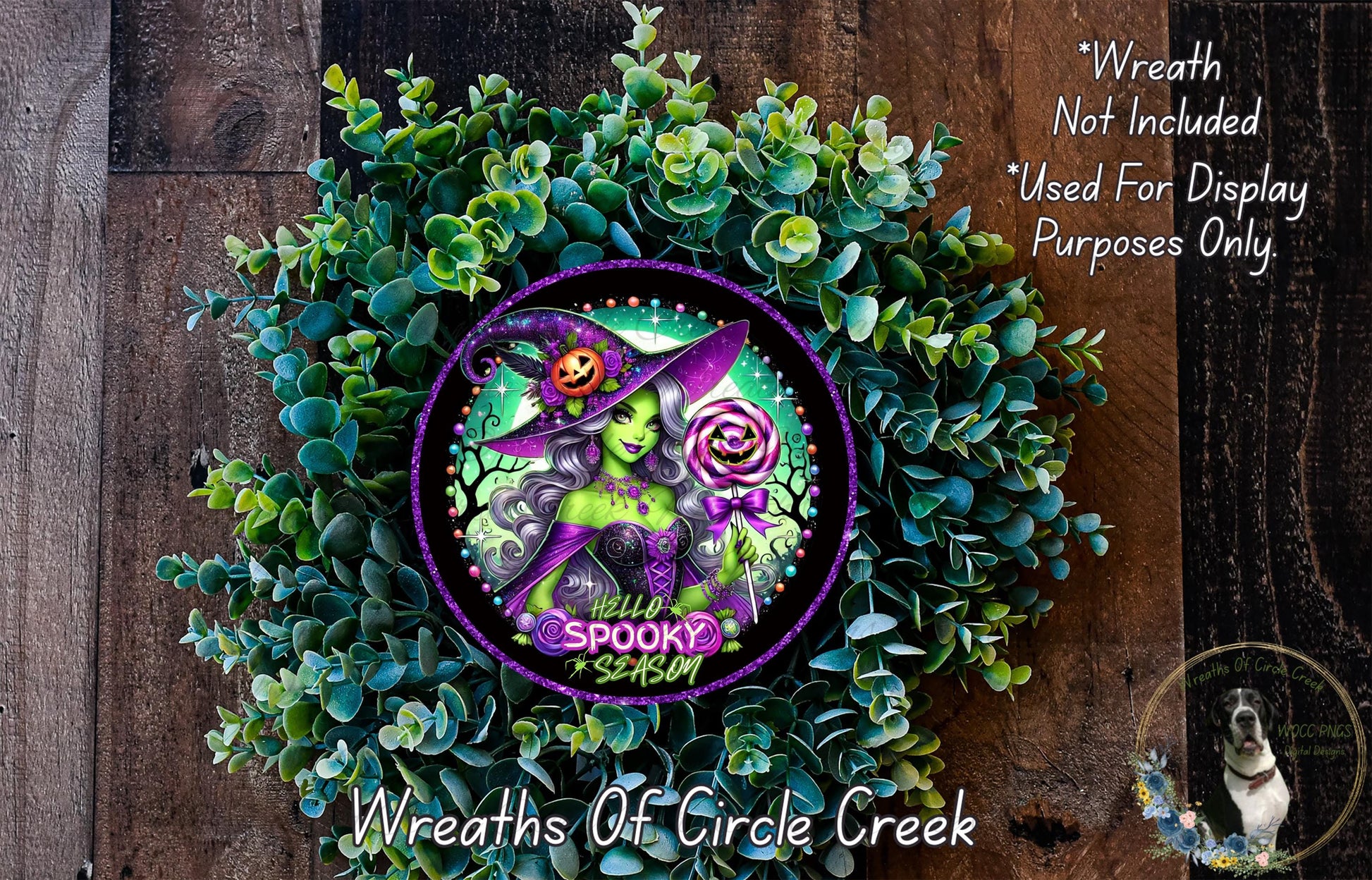 a wreath with a witch on it, surrounded by greenery. The wreath has a purple border and a purple and green design. The text above the wreath says "Wreath Not Included * Used For Display Purposes Only".
