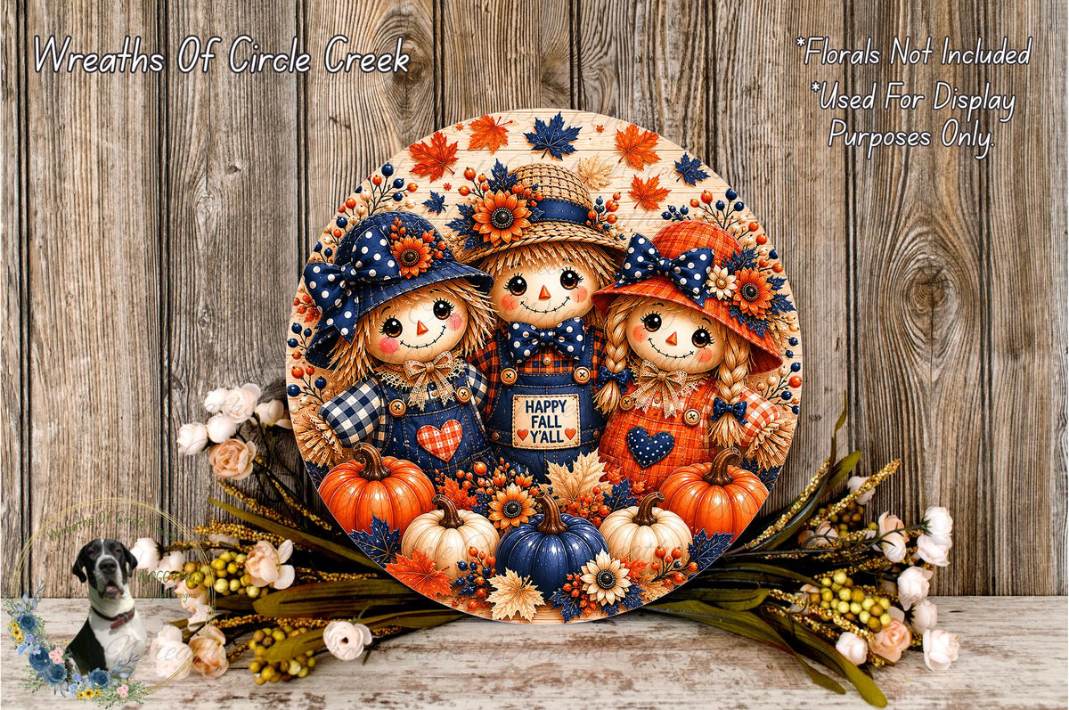 A decorative wreath featuring three scarecrow dolls, surrounded by pumpkins, flowers, and autumn leaves, with the text "Happy Fall" displayed on the wreath.