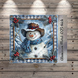A snowman wearing a hat and scarf, surrounded by holly leaves and berries, is depicted in a decorative frame against a snowy winter landscape.